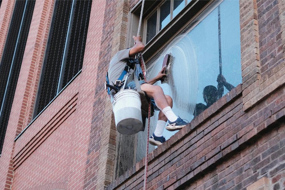 man cleaning a window while hanging from a rope